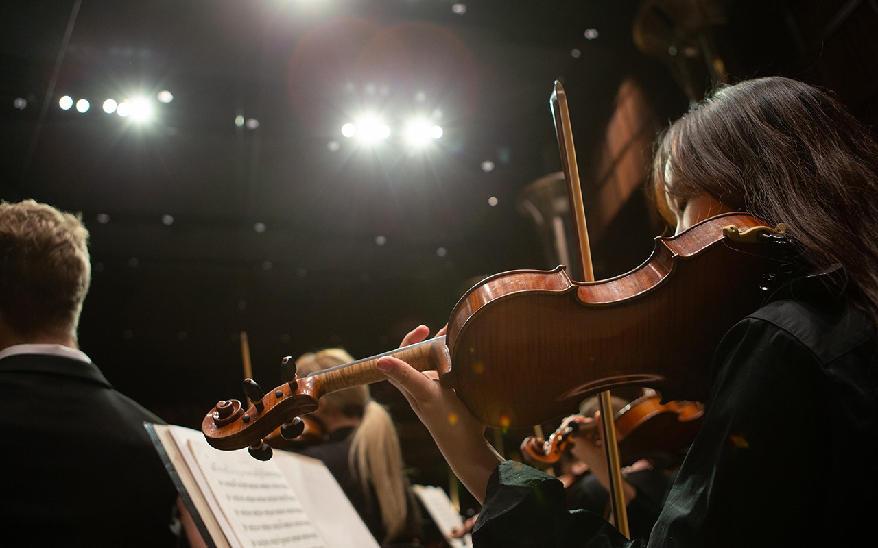 Female violin student performs onstage under lights with the CCM Concert Orchestra
